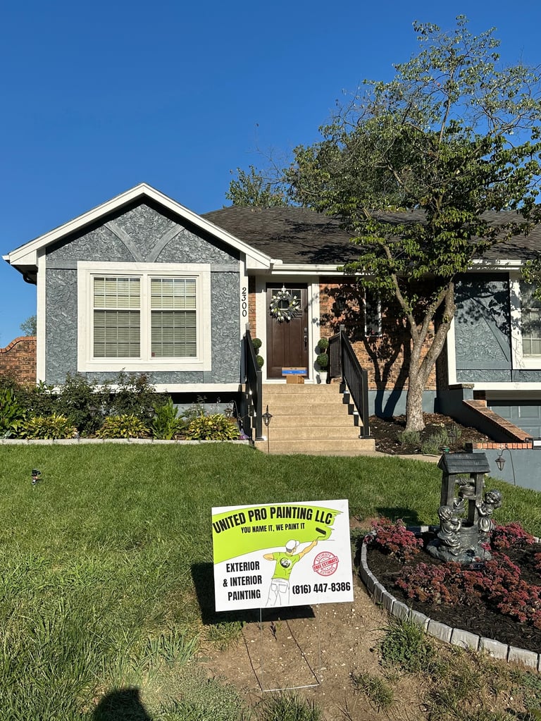 Blue and white single-story house with a large tree in front and a yellow contractor sign in the yard